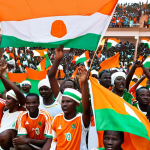 **Soccer Culture in Niger**: Create an image depicting a vibrant soccer match in Niger, showcasing enthusiastic fans in the stands, waving flags and cheering. The players on the field should display intense expressions of determination as they compete. Include elements of national pride, such as jerseys featuring the Niger flag.